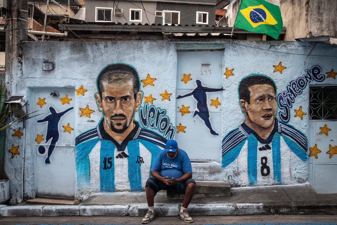 Un hombre sentado frente a su casa con la pared pintada con las imágenes de los exjugadores argentinos Verón y Simeone hoy, en la comunidad de Dendê, en Río de Janeiro (Brasil). EFE/ André Coelho